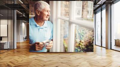 senior man holding cup and looking out of the window Wall mural