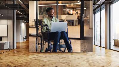 Smiling african american businessman with disability using laptop in wheelchair Wall mural