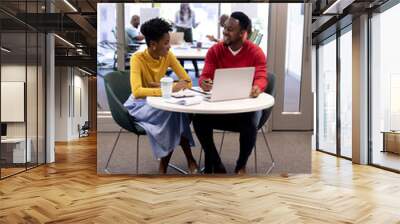 Smiling african american female and male advisors planning strategy together with laptop at office Wall mural