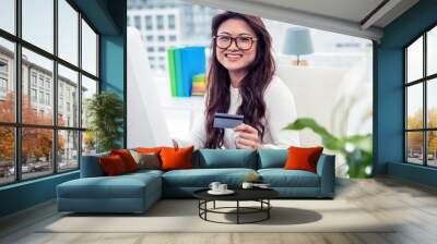 Smiling Asian woman on computer holding credit card Wall mural