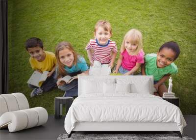 Smiling classmates sitting in grass and holding books Wall mural