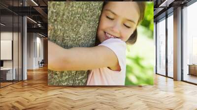 Smiling girl hugging tree with eyes closed at park Wall mural