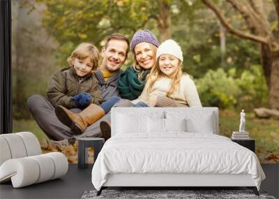 Smiling young family sitting in leaves Wall mural