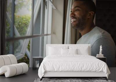 Thoughtful smiling man looking out through window at home Wall mural