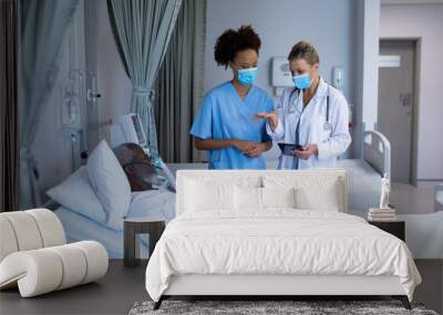 Two diverse female doctors talking to african american male in hospital patient room Wall mural