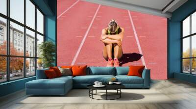 Upset female athlete sitting on running track Wall mural