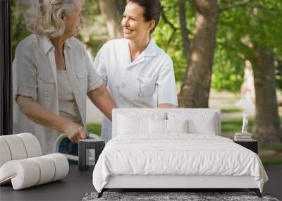 Woman assisting mature female with walker at park Wall mural