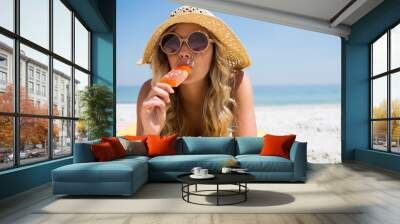 Woman eating popsicle while relaxing at beach Wall mural