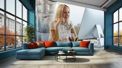 Woman holding eyeglasses at desk in office Wall mural