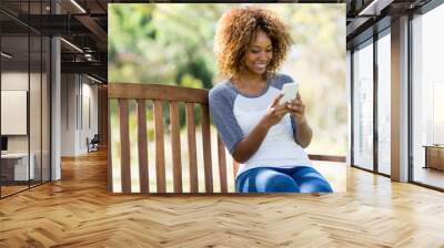 Woman using mobile phone while sitting on the bench Wall mural