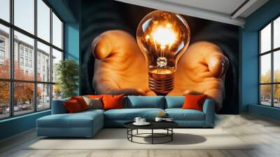 A glowing light bulb is cradled in two hands, symbolizing innovation, inspiration, and the power of ideas. Wall mural