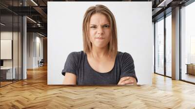 Angry young female with dark eyes frowning her nose and lips wearing casual T-shirt standing crossed hands isolated over white background showing her dissatisfaction. People and emotions concept Wall mural