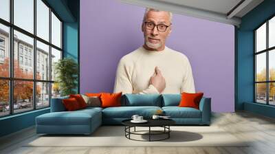 Are you talking about me? Bearded senior man points at himself with bewilderment, asks if he did something wrong, wonders, wears casual white jumper and spectacles, isolated over purple background Wall mural