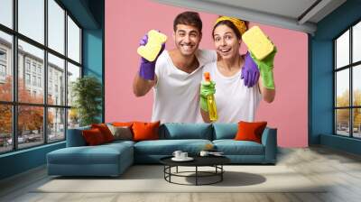 Attractive cheerful young European male and female cheering after they finished cleaning up the rooms, smiling, holding sponges and spray detergent, feeling happy and carefree. Body language Wall mural