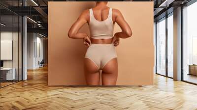 Back view of sensual slim woman poses in panties and top has perfect figure healthy dark skin isolated on brown background. Perfect female body Wall mural