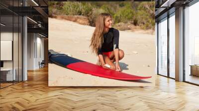 Beautiful cheerful surfing girl waxes surfboard with wax, prepares for real collasping waves, poses on empty beach, has pleasant appearance, looks aside happily. Healthy lifestyle, vacation, hobby Wall mural