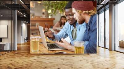 Business partners meeting together at cafeteria, developing business strategy using laptop computer, pointing at screen with hands, discussing something important. Black male showing presentation Wall mural