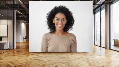 Carefree and relaxed pretty young mixed race female wearing big round eyeglasses smiling broadly, feeling excited about spending vacations abroad, standing isolated at white blank studio wall Wall mural