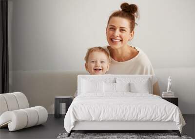 charming brunette woman playing with her baby while sitting on a bed in her apartment at the weekend Wall mural