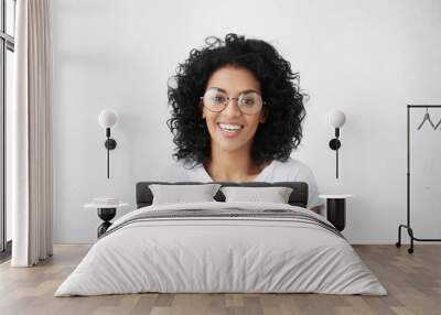 Close up isolated studio shot of good looking cheerful positive young mixed race female with brunette curly hair, smiling broadly, showing her white teeth at camera while having fun indoors Wall mural