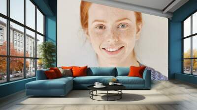 Close up portrait of beautiful young redhead model with different colored eyes and healthy clean skin with freckles smiling joyfully, showing her white teeth, posing indoors. Heterochromia in human Wall mural