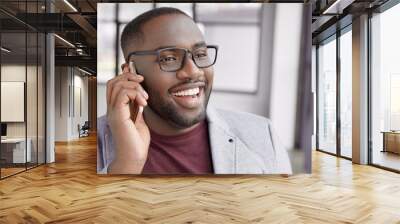 Close up portrait of cheerful male with dark pure healthy skin, has broad smile, shows perfect teeth, speaks over smart phone, call to secretary assistant, arrange conference meeting to sum up work Wall mural