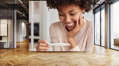 Close up shot of happy future mother smiles broadly when finds out positive results of pregnancy test, cant believe in such good news, poses against cozy domestic background. Yes, I am pregnant! Wall mural