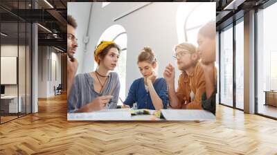 Collaboration and brainstroming concept. Portrait of interracial friends gathering together sitting at table in classroom surrounded with books having debates expressing their opinions and views. Wall mural