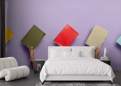 Collage image of various colorful textbooks in male hands isolated over purple background. Books for studying. Education concept. Notepads for writing notes with colored bookmarks. Horizontal shot Wall mural