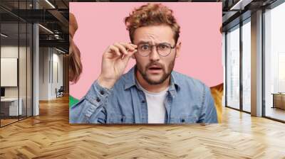 Composition of five different people wear spectacles, look with surprised expression, beig from various nations, express shock and disbelief. Women and men stand in row isolated on pink background Wall mural