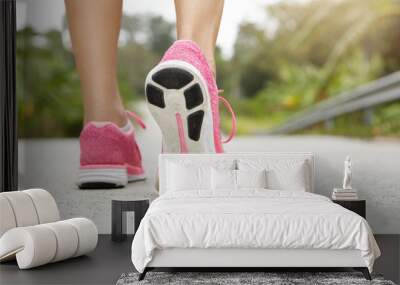 Cropped rear shot of athletic girl wearing pink sneakers while hiking or jogging on pavement outdoors. Woman jogger with fit beautiful legs doing workout. Selective focus, freeze action shot Wall mural