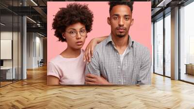 Cropped shot of serious black female and male partners have thoughtful expressions, think about new project, isolated over pink background. Dark skinned colleagues stand indoor. Togetherness concept Wall mural