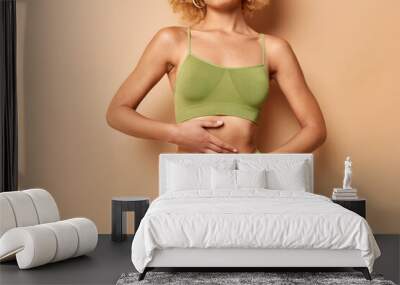 Cropped view of unrecognizable fit woman wears green top and panties keeps hands on flat belly poses against brown background shows perfect body after diet. Empty space for your advertisement Wall mural