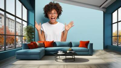 curly optimistic woman raises palms from joy, happy to receive awesome present from someone, shouts  Wall mural