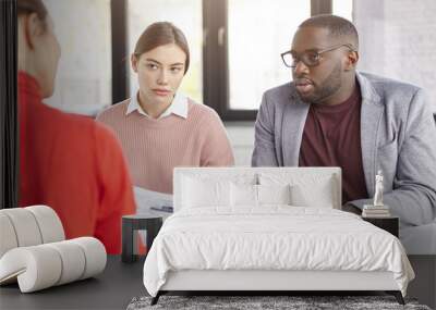 Dark skinned male and females coworkers sit together at working place, discuss opinions and ideas for new startup, plan strategies, have serious looks. Diverse crew of office workers have meeting Wall mural