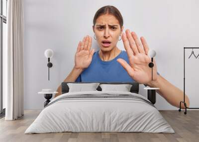 Do not come closer. Displeased woman shows her denial opinion says stay away from me calm down or slow asks to keep distance demonstrates taboo gesture dressed casually isolated over white wall Wall mural