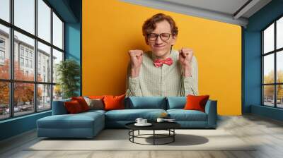 Ecstatic male nerd raises clenched fists, believes in success, closes eyes and awaits announcement of results, participates in contetst, hopes to win, expresses impatience, dressed formally. Wall mural