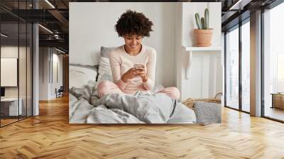 excited delighted dark skinned housewife enjoys rest in bed, watches video via media app, has spare  Wall mural