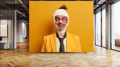 Funny positive bruised man has good sense of humor, got traumas after boxing with someone, doesnt care about injuries, wears medical bandage on hurt head, isolated on yellow studio background Wall mural