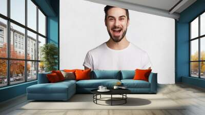 Glad bearded young male happy to have date with girlfriend, being in hgh temper or good mood, dressed casually, isolated over white studio background. Shot of excited unshaven happy man indoor Wall mural