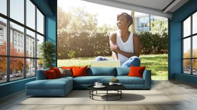 Happy and cheerful black female with short haircut sitting on the grass, smiling to her friends approaching her. Young African student using her notebook outdoor, resting after a hard day at college Wall mural