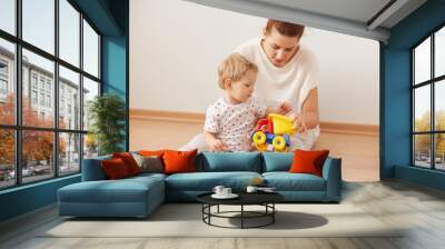 Happy family enjoying free time at home in sweet morning, sitting on the floor against white background, playing with toys. Caring young mother with her cute son spending weekend together Wall mural