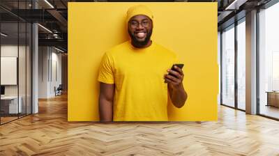 Happy handsome overweight man being in high spirit, checks messages and talking with friend in social networks, makes new appointment, dressed in casual bright outfit. Yellow colour prevails Wall mural