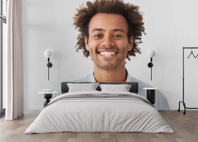 Headshot of handsome mixed race young man with shining smile, looks positively at camera, has white perfect teeth, stands against white background. People, lifestyle, emotions and fun concept Wall mural