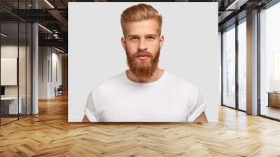 Headshot of red haired serious young male blogger looks confidently at camera, thinks about new content of his web page, dressed casually, earns money distantly, isolated over white background Wall mural