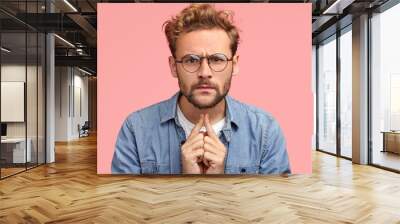 Headshot of serious intelligent young male proffesor listens something with attentive look, has scrupulous gaze directly into camera, dressed in fashionable outfit, isolated over pink background Wall mural