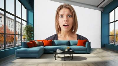 Horizontal portrait of cute young woman wearing casual sweater looking at camera with wide open mouth and eyes being astonished isolated over white background. Surprised woman posing in studio Wall mural