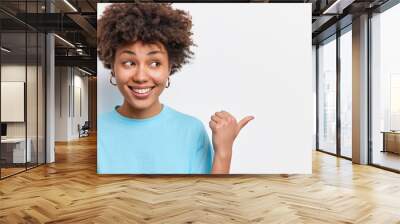 Horizontal shot of cute pleased Afican American woman shows store promo deal smiles positively points at right copy space isolated over white background shares good news with you. Check this out Wall mural