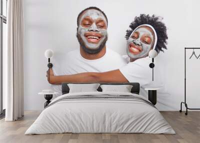 Horizontal shot of happy Afro American woma embraces her brother with love wear clay face masks take care of complexion wear casual t shirts smile broadly being in good mood. Relationship concept Wall mural