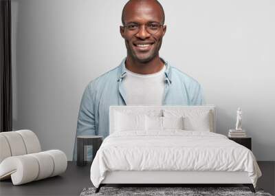 Horizontal shot of happy dark skinned male with positive smile on face, being in high spirit as achieves success in business sphere, dressed in casual outfit, isolated over white background. Wall mural